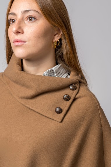 Poncho castanho com gola alta e três botões decorativos, usado sobre camisa branca quadriculada