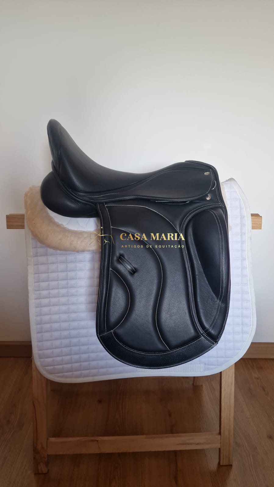 Selim de equitação preto sobre manta branca em cavalete de madeira.
