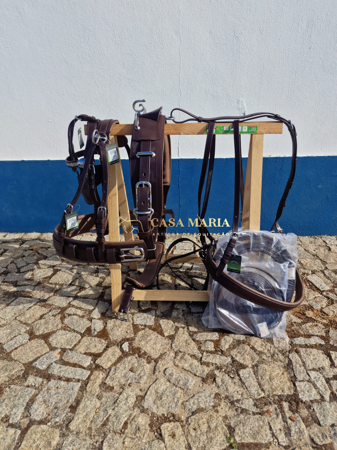 Equipamento de equitação em cabedal castanho pendurado em suporte de madeira com chão de calçada