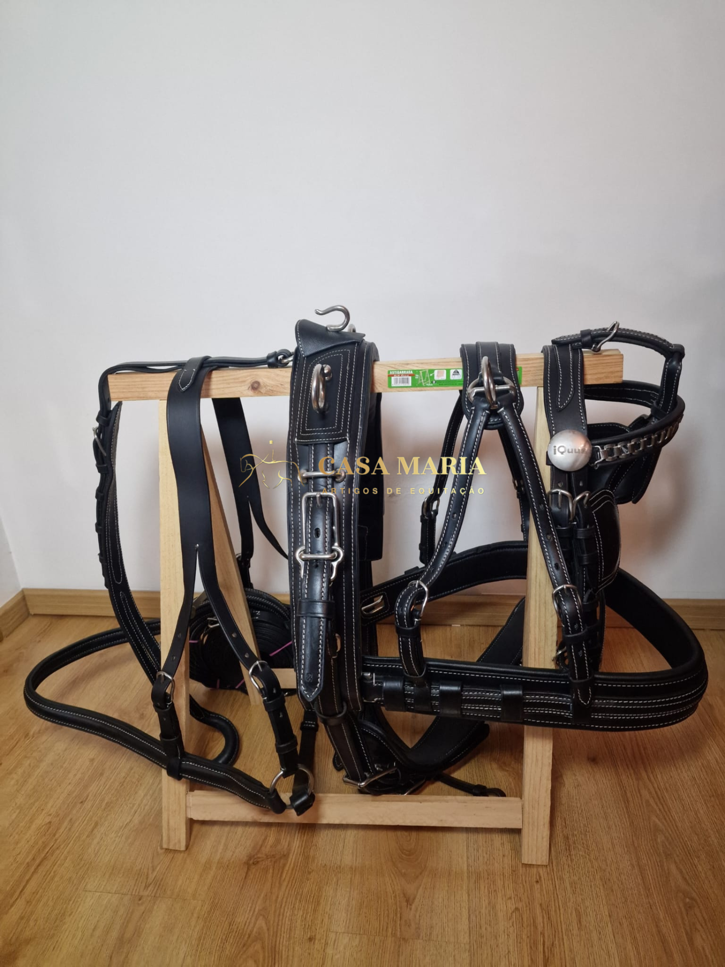 Arreios em pele preta com costuras brancas pendurados em estrutura de madeira