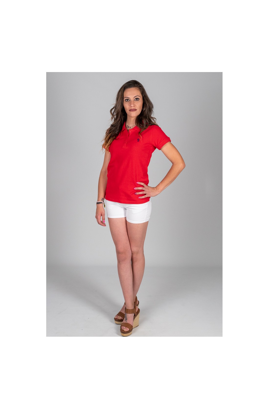 Mulher com t-shirt vermelha, calções brancos e sandálias castanhas em fundo cinzento