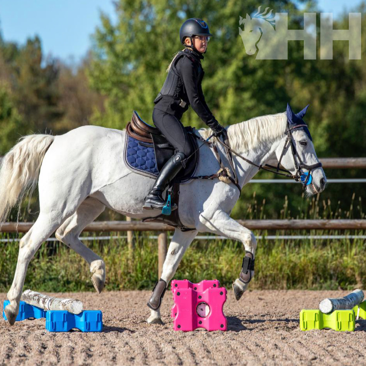 Cavalo branco a saltar obstáculos coloridos em areia com cavaleiro embutido.