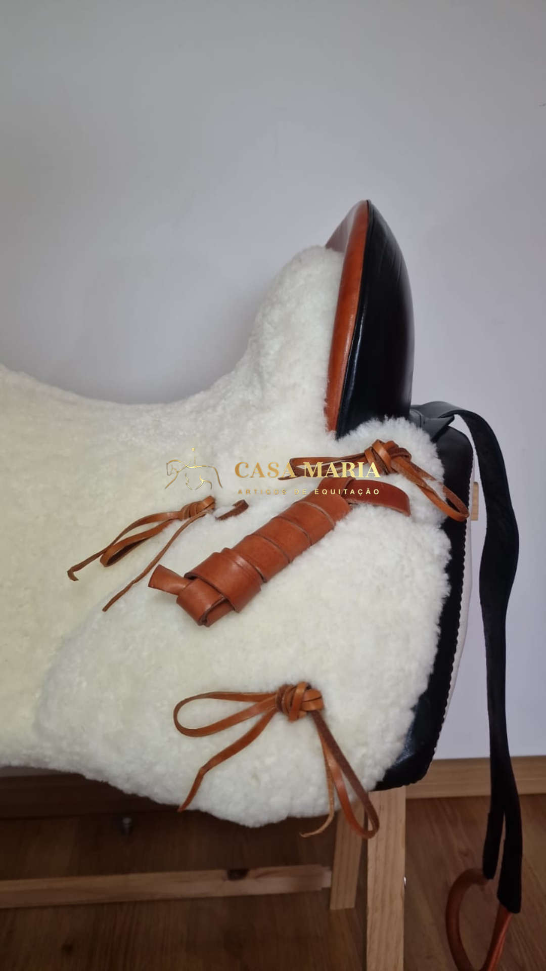 Sela de equitação com pelo branco e couro castanho e preto com texto CASA MARIA ARTIGOS DE EQUITAÇÃO