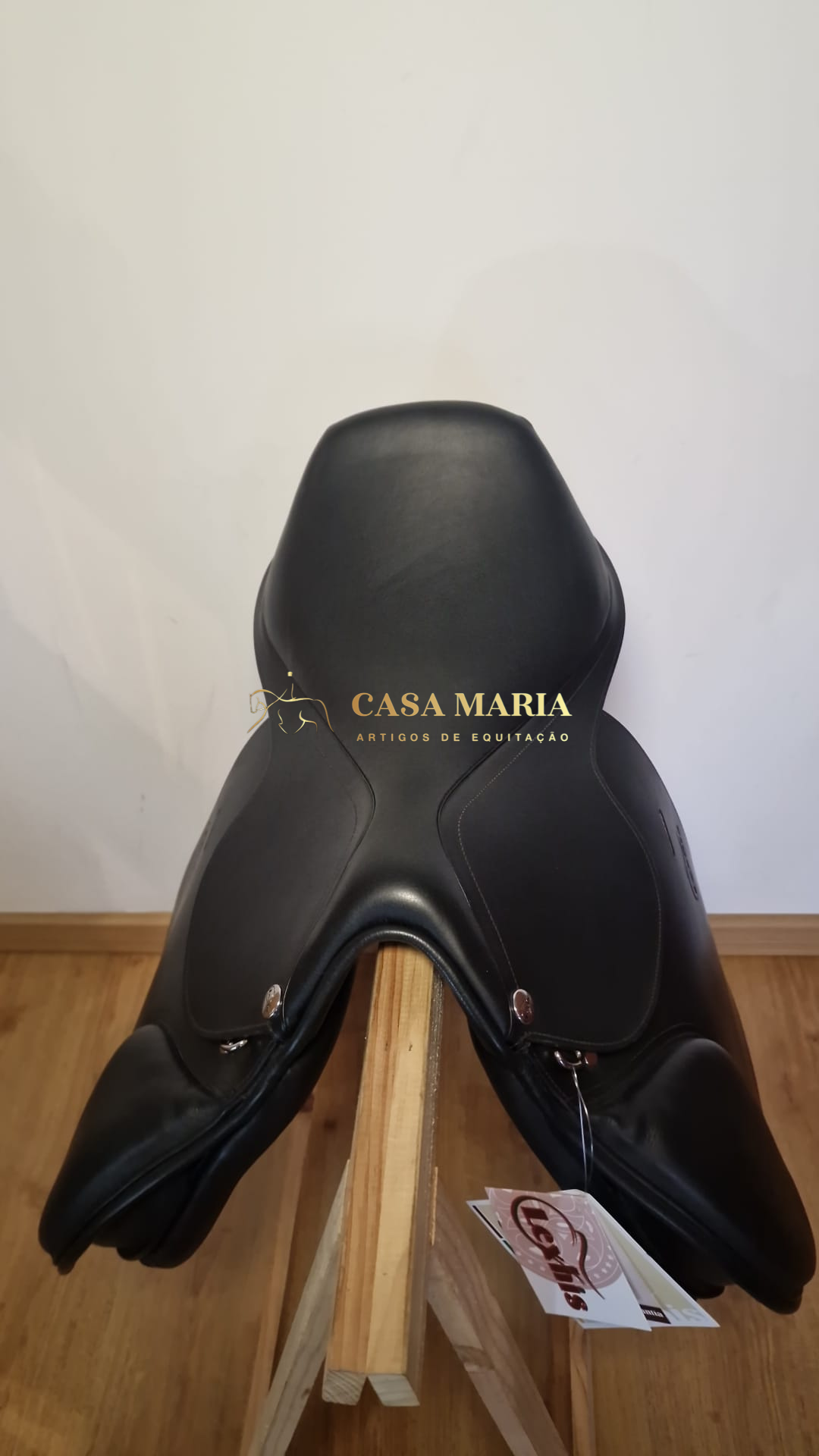 Sela de equitação preta em couro com etiquetas penduradas sobre suporte de madeira