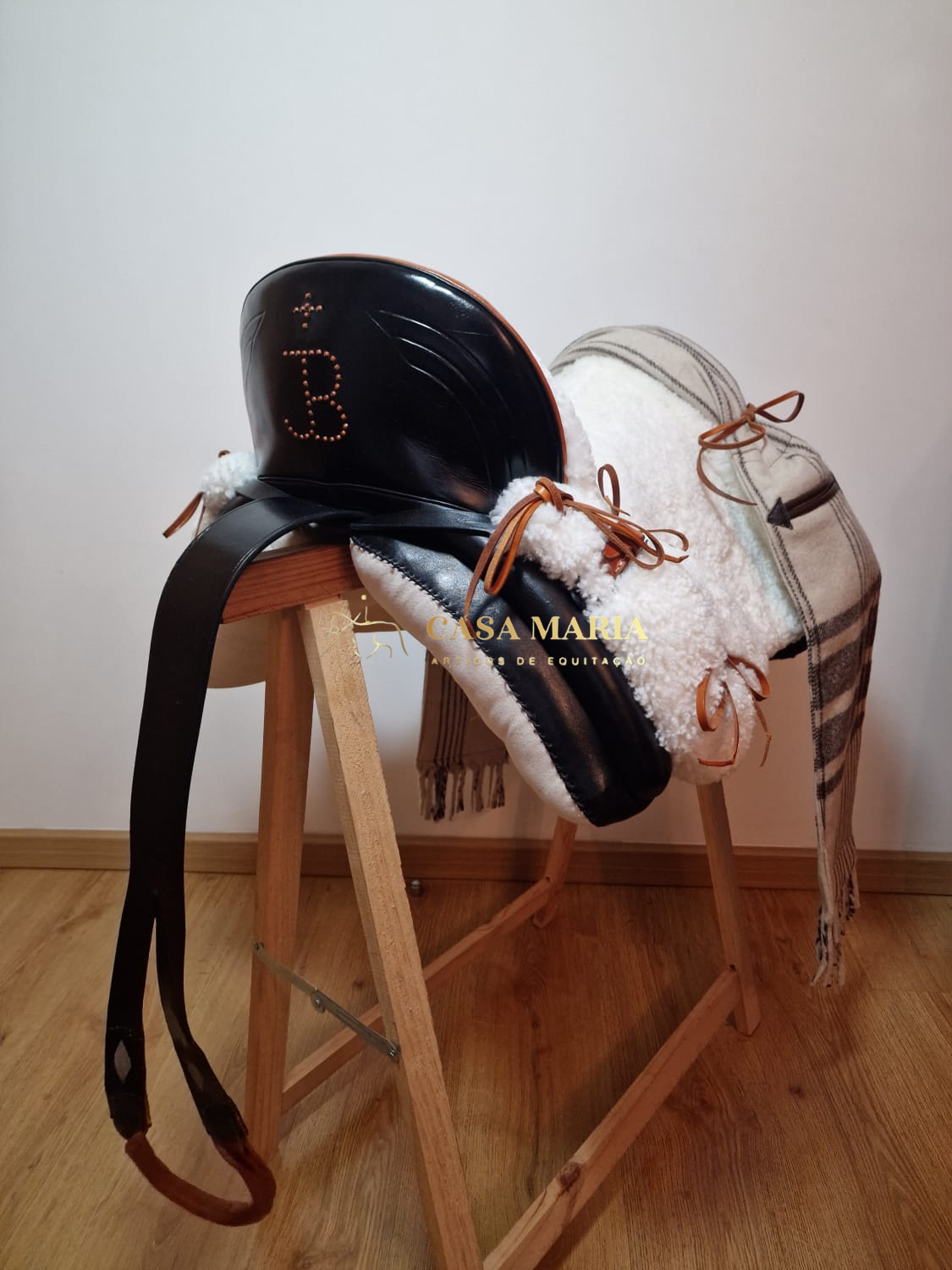 Sela de equitação preta com pele sintética branca e manta xadrez em suporte de madeira