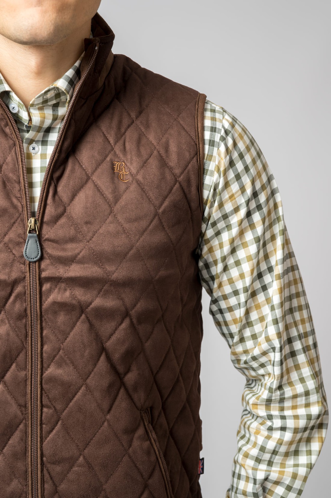 Colete castanho acolchoado com camisa xadrez ao fundo cinza
