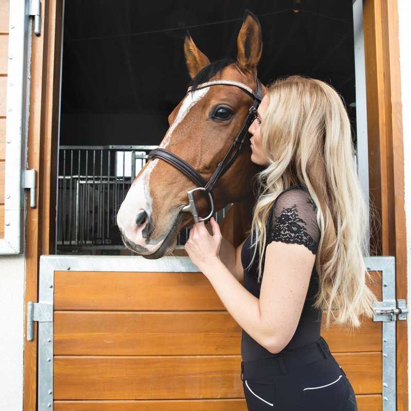 Mulher loira com cavalo castanho ao lado de porta de madeira em estábulo