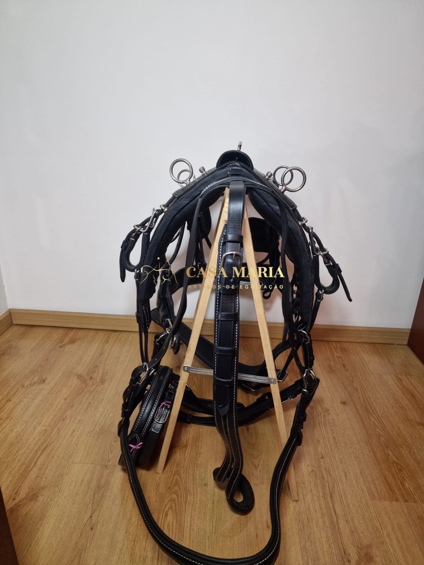 Arnês em couro preto com fivelas e argolas pendurado num suporte de madeira