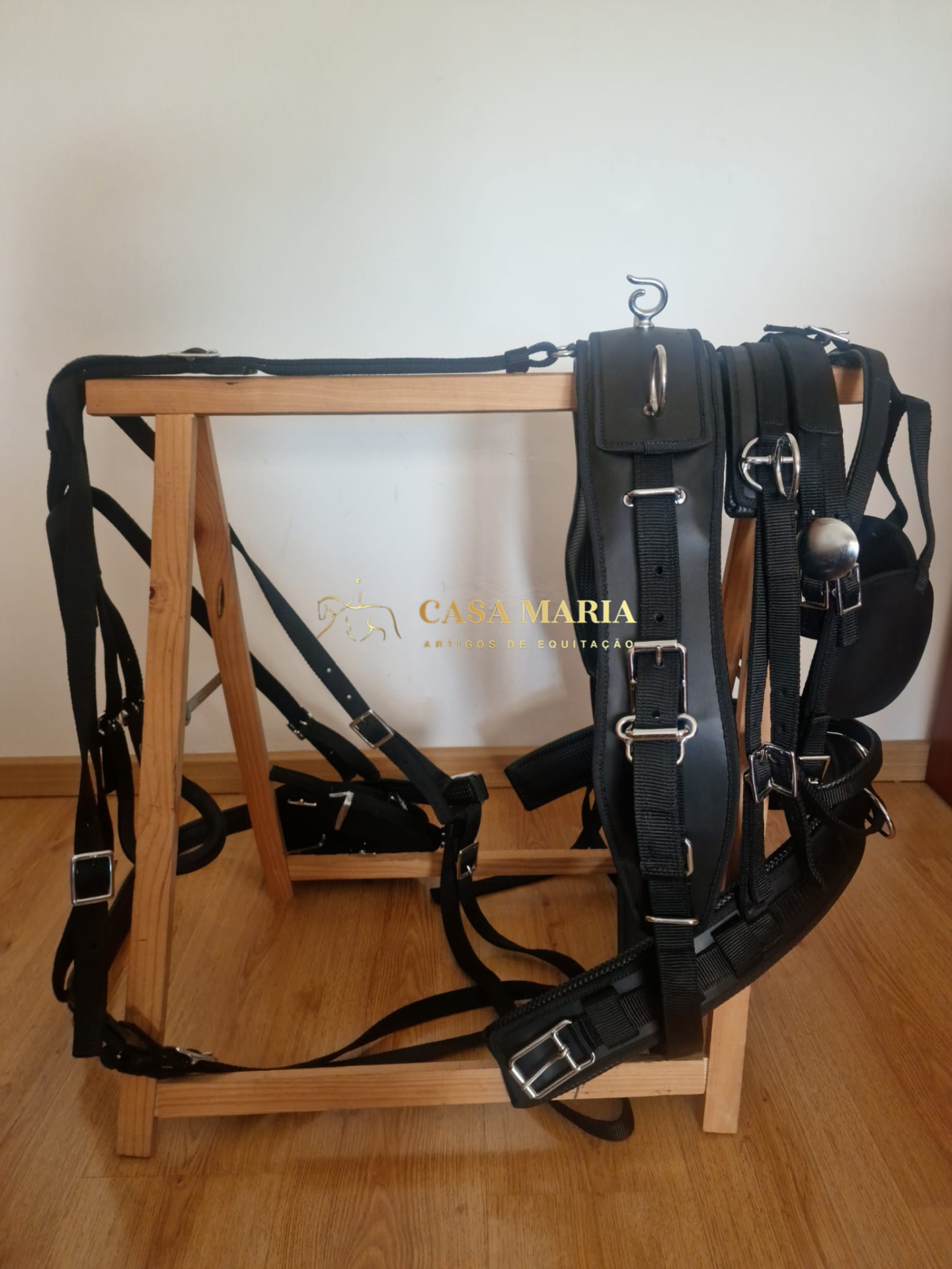 Arnês preto de equitação com fivelas prateadas em suporte de madeira