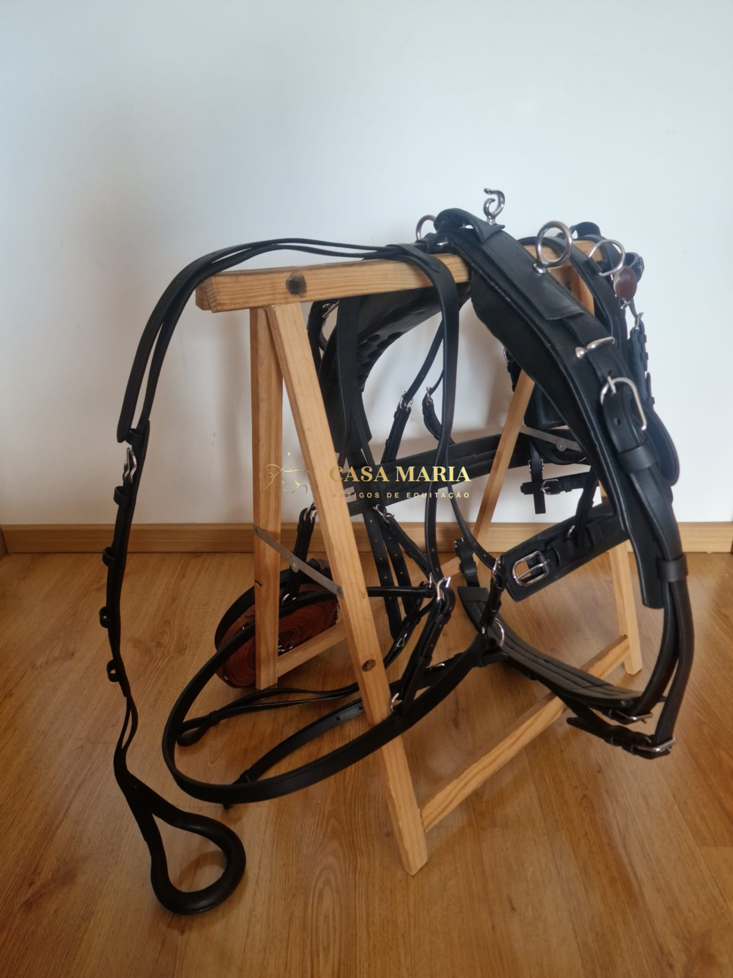 Arreio e cabeçada de couro preto com fivelas metálicas em suporte de madeira