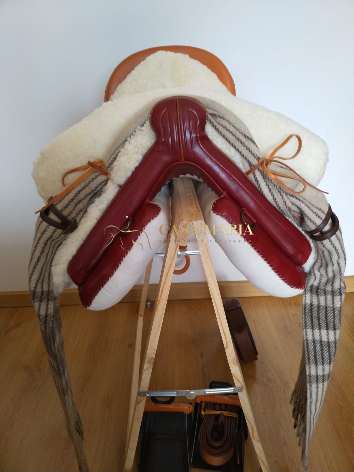 Sela de equitação com manta xadrez pendurada num suporte de madeira