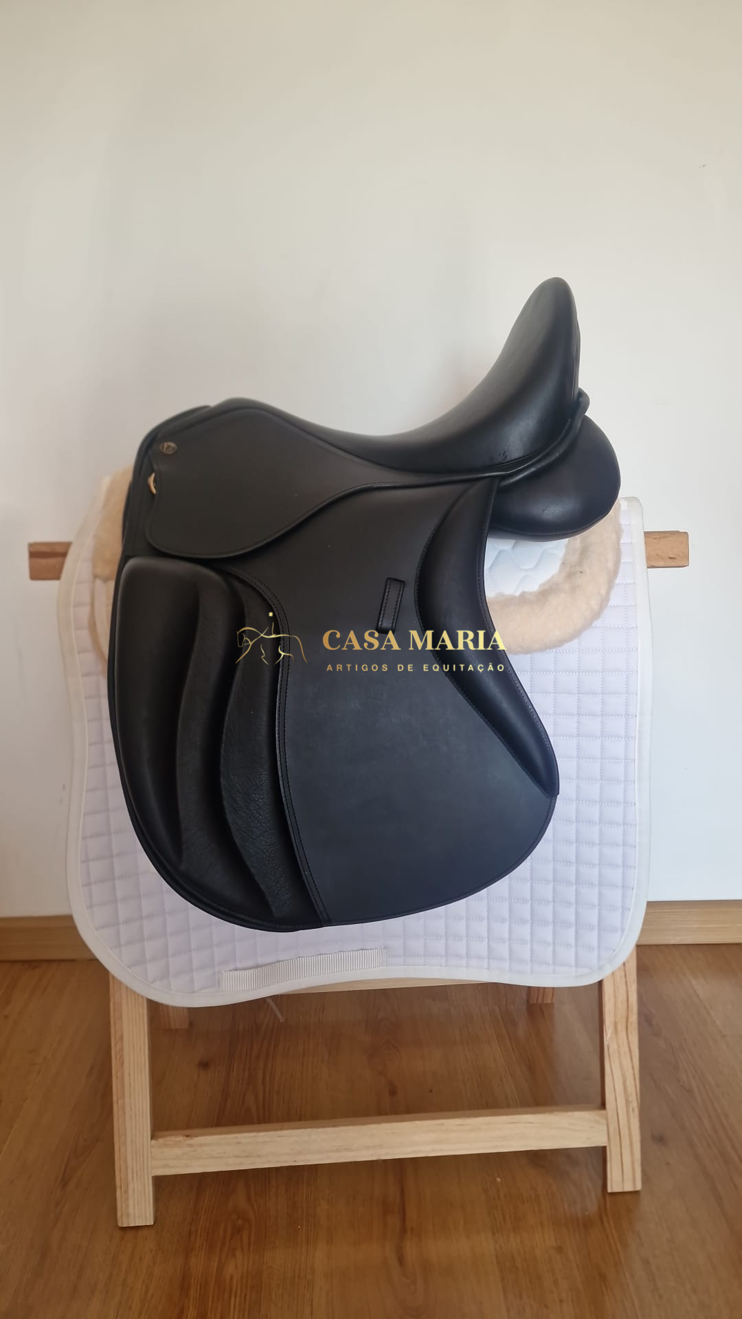 Sela de cavalo preta em couro sobre manta branca e suporte de madeira