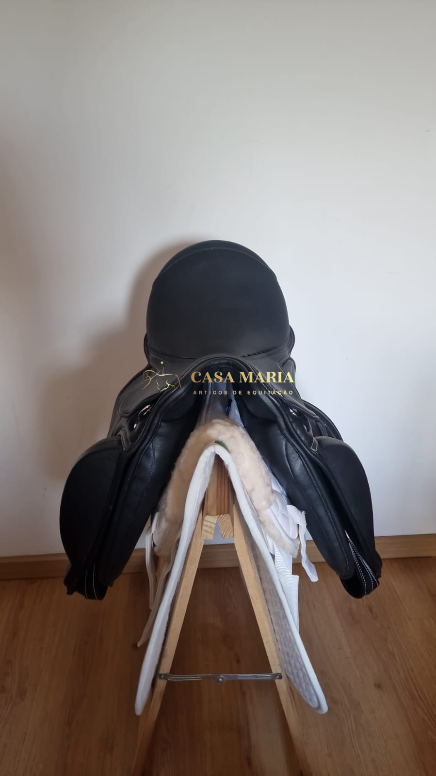 Sela de equitação preta com pele branca sobre suporte de madeira e capacete preto