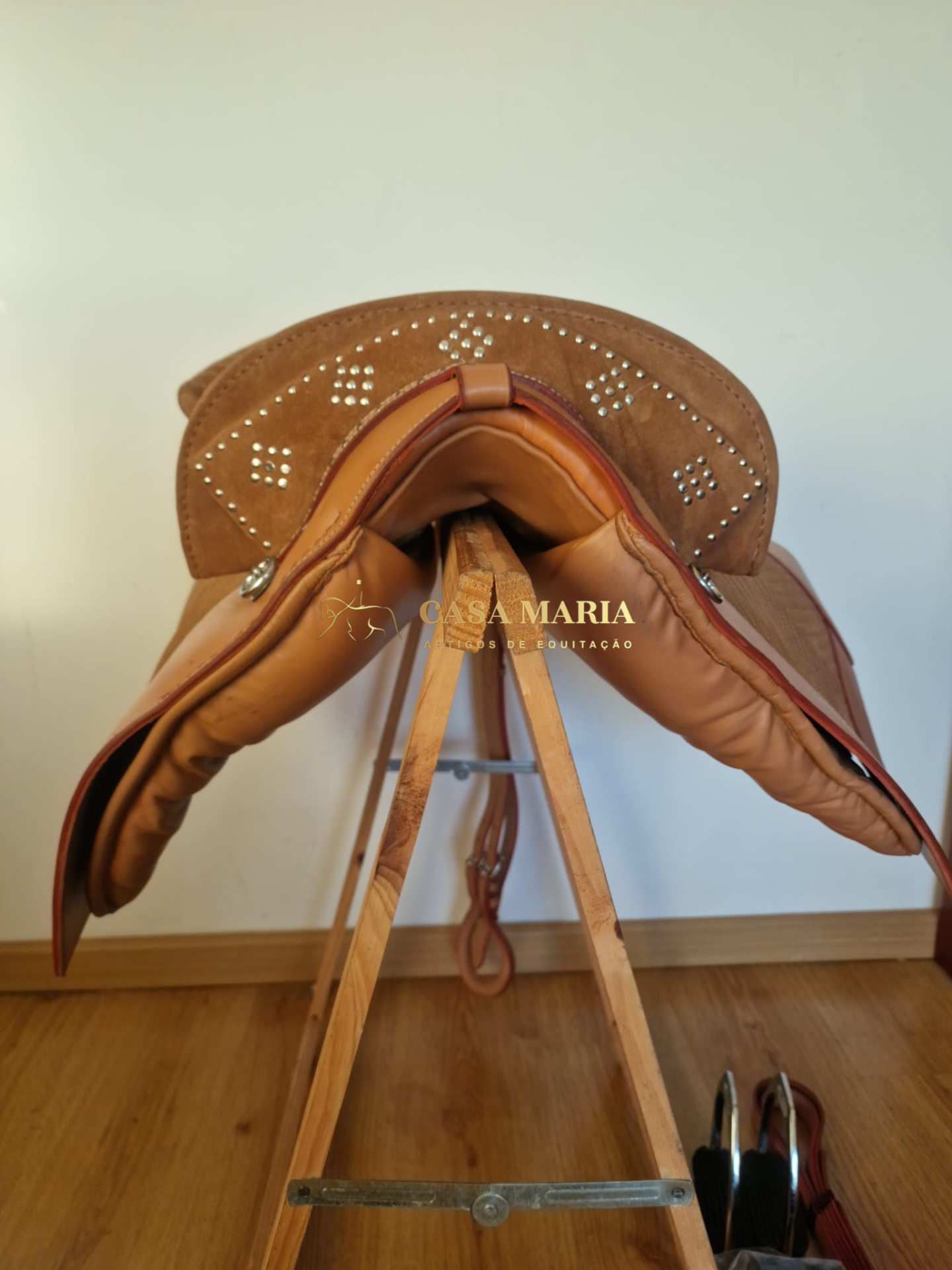 Sela de cavalo castanha com detalhes em camurça e tachas sobre suporte de madeira