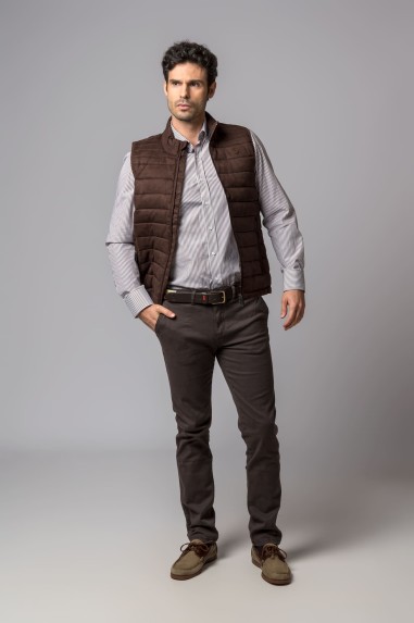 Homem com colete acolchoado castanho e roupa casual em fundo cinza