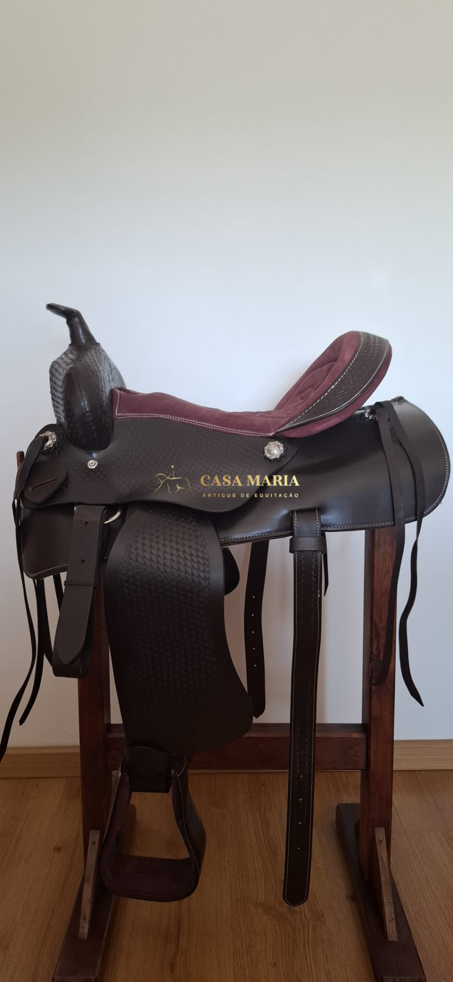 Sela de equitação em couro preto com assento bordô sobre suporte de madeira