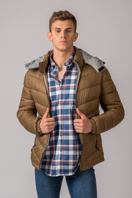 Homem com casaco puffer castanho e capuz cinzento, camisa xadrez e jeans.