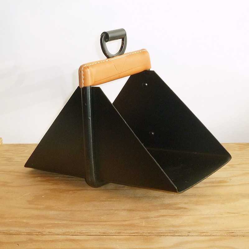 Recipiente triangular preto com alça de couro castanho sobre mesa de madeira.