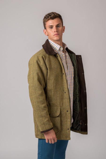 Homem com casaco verde-limão de risca, camisa xadrez e calças azuis num fundo cinzento.