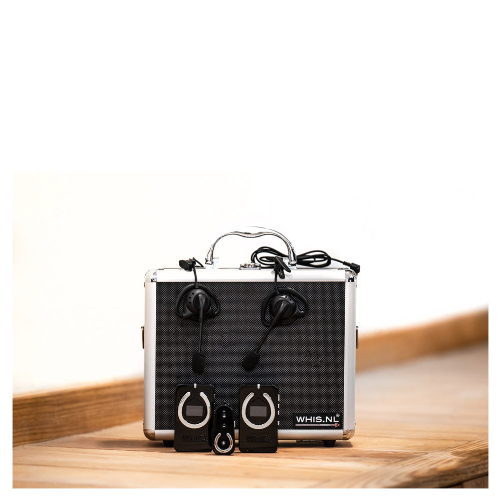 Maleta metálica prateada com transmissores e auscultadores pretos em cima de mesa de madeira