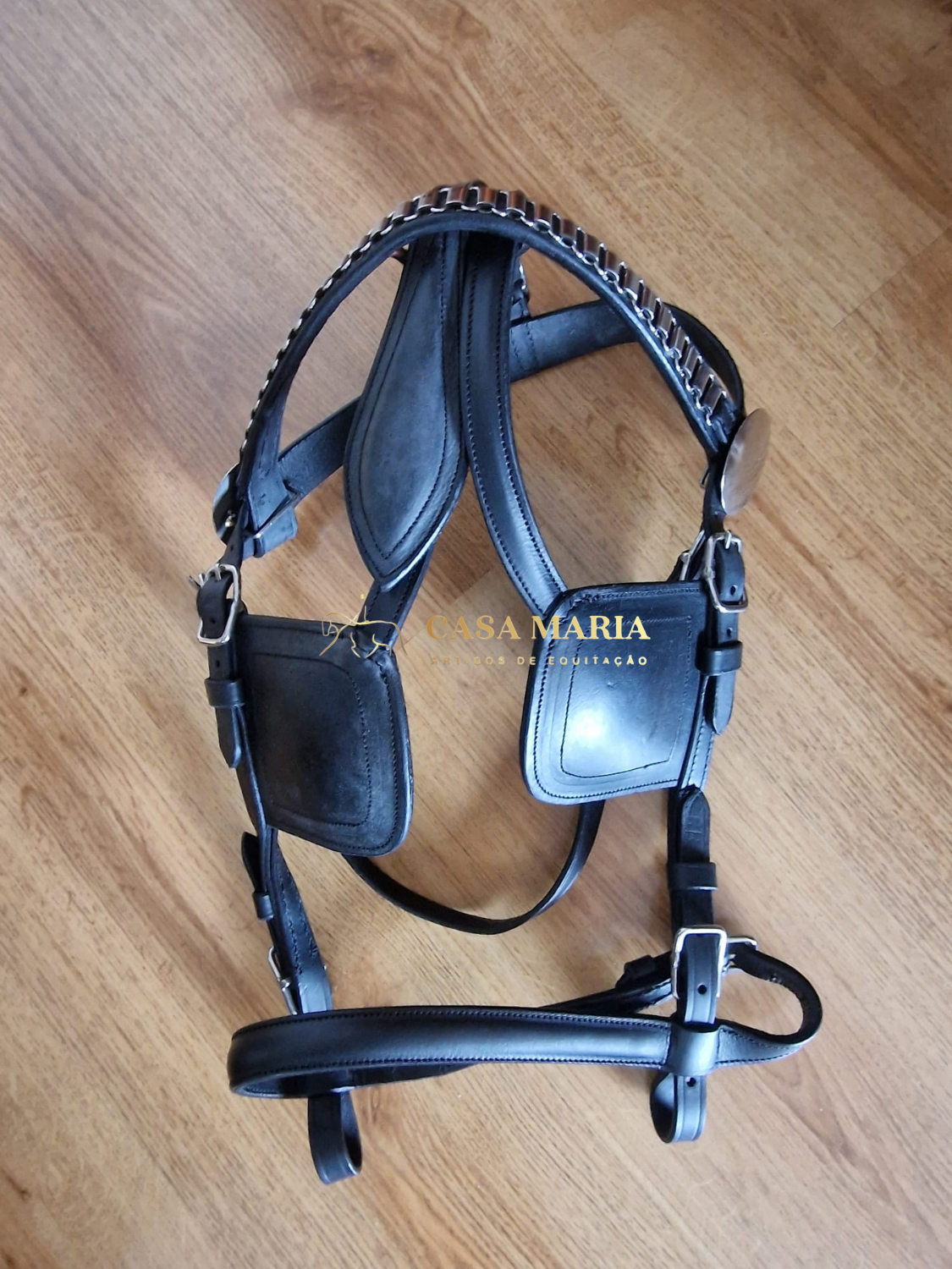Bridão em pele preta com pormenores em metal prateado sobre chão de madeira clara
