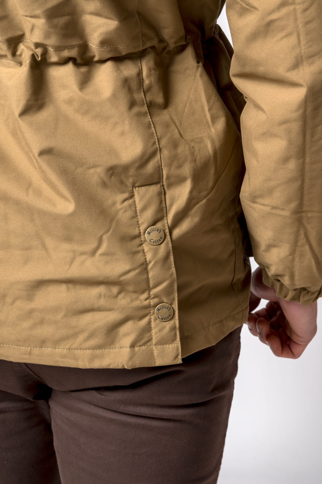 Detalhe de peça de roupa castanha clara com botões metálicos British Cotton.