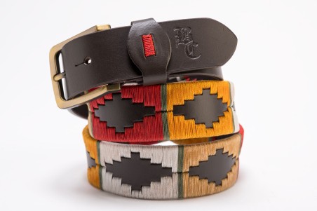 Três cintos, dois coloridos com padrão geométrico e um castanho de pele com fivela metálica.