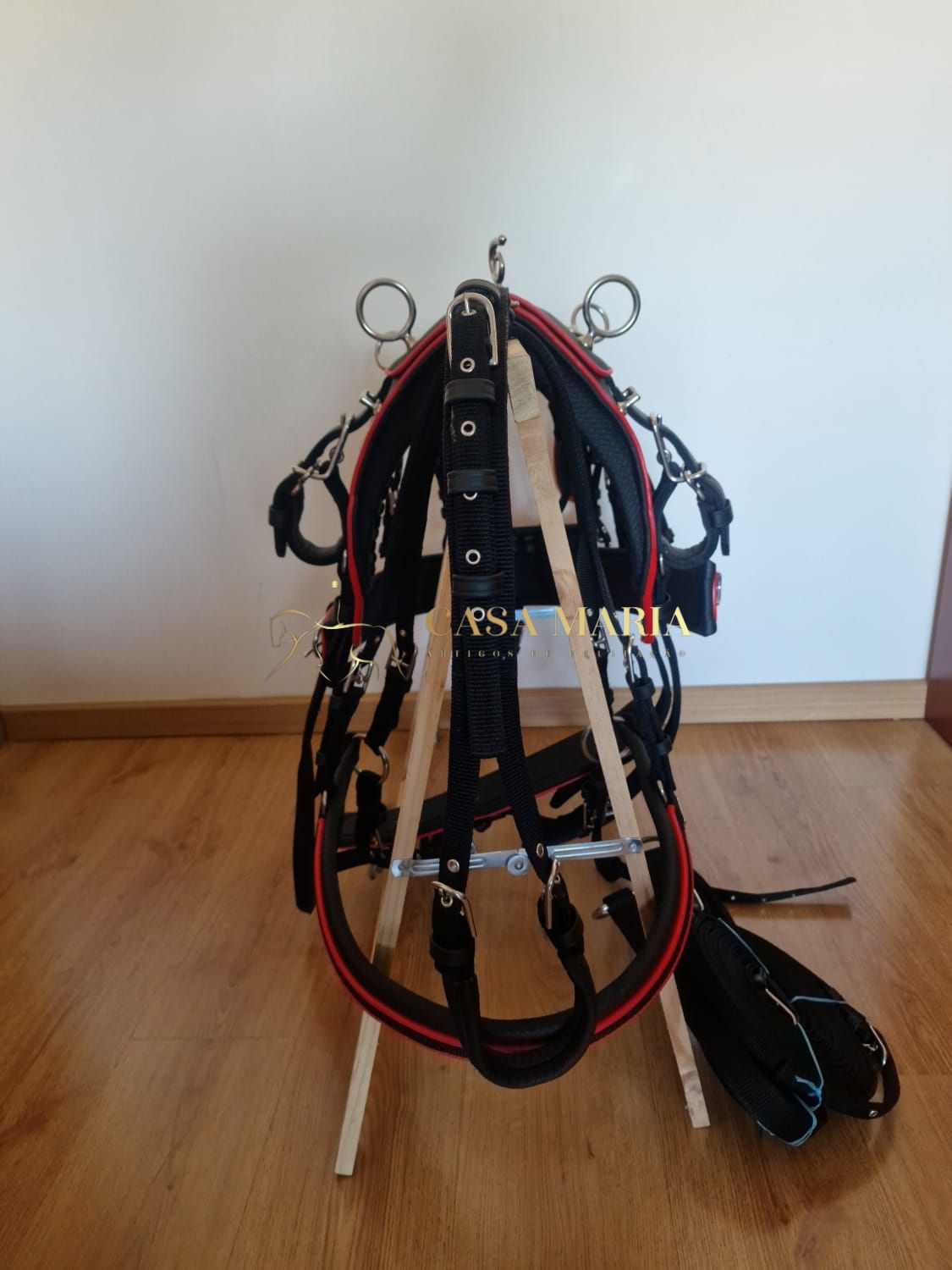Arreio de equitação preto com detalhes vermelhos em suporte de madeira