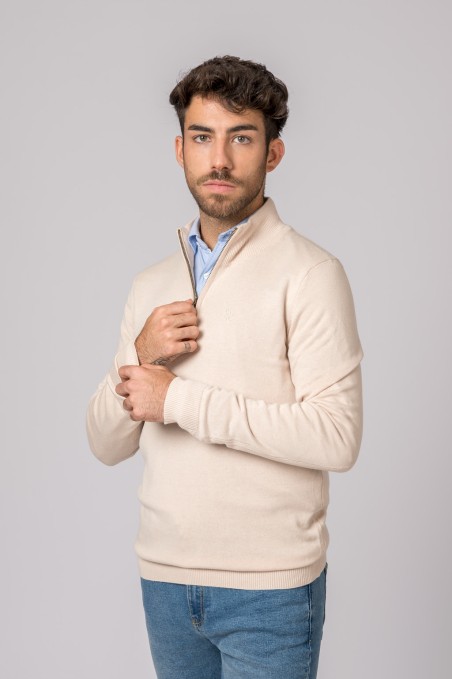 Homem com camisola bege de meia gola e calças de ganga azul
