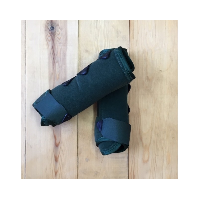 Par de protetores de canela verdes de tecido acolchoado com fechos pretos sobre chão de madeira