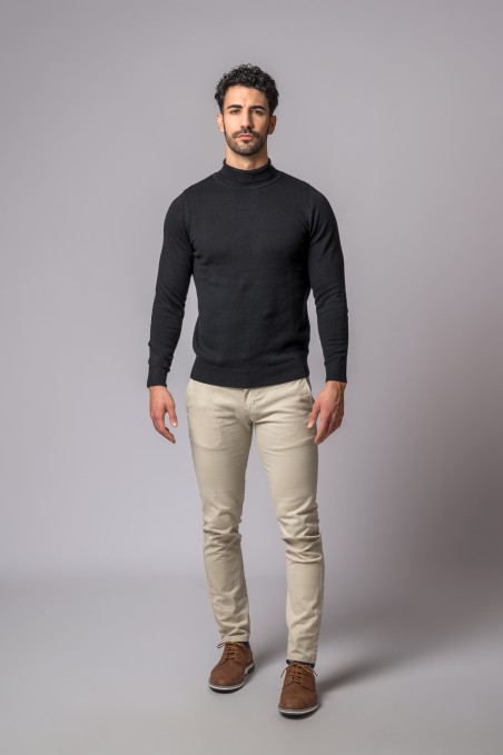 Homem com camisola preta de gola alta, calças bege e sapatos castanhos em fundo cinza