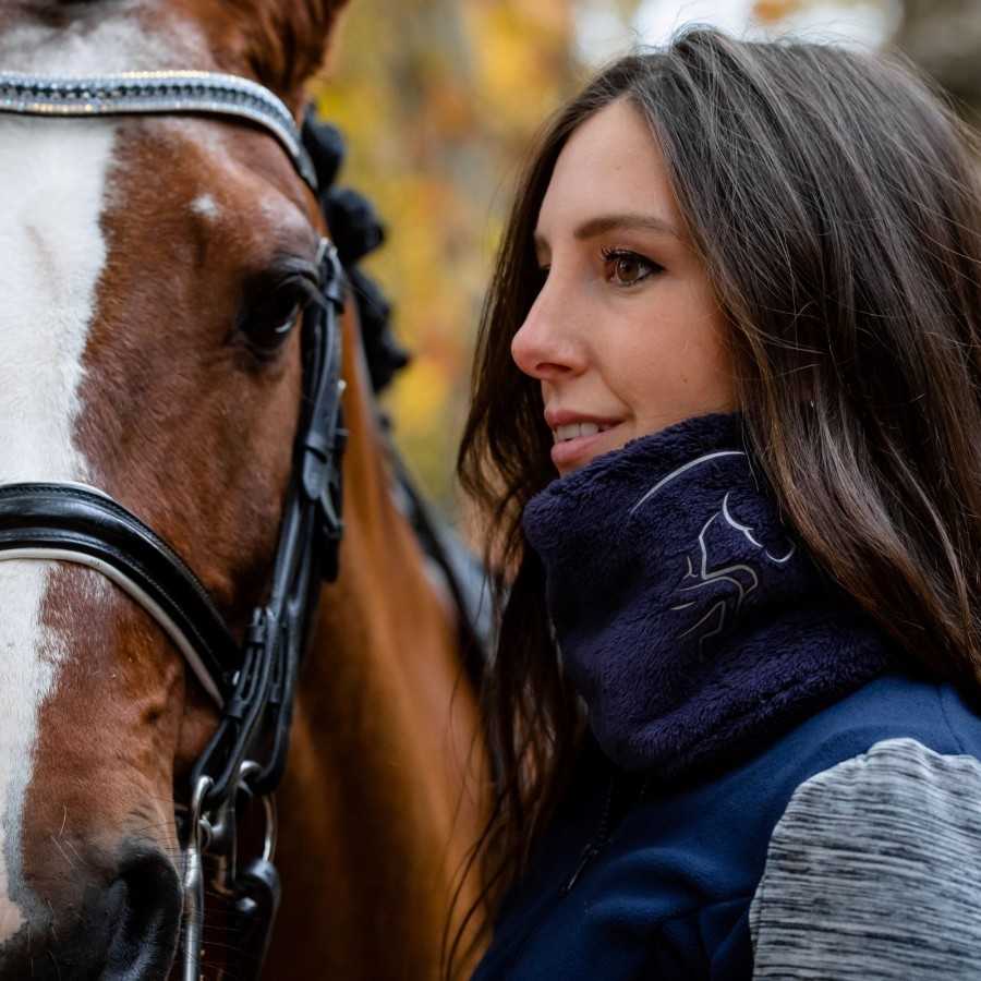 Mulher com colarinho felpudo azul escuro com padrão branco ao lado de cavalo castanho com listra branca e sela preta