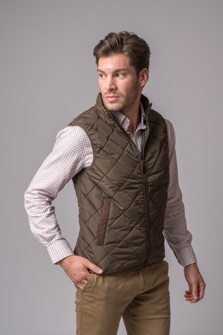 Homem com colete acolchoado verde-oliva e camisa xadrez de fundo cinza