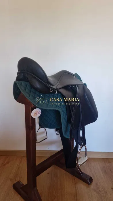 Sela de equitação preta em couro sobre manta verde escura em suporte de madeira.