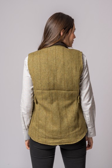 Mulher vista de costas a usar colete em tecido tweed castanho claro, camisa branca com padrão de quadrícula castanha e calças pretas.