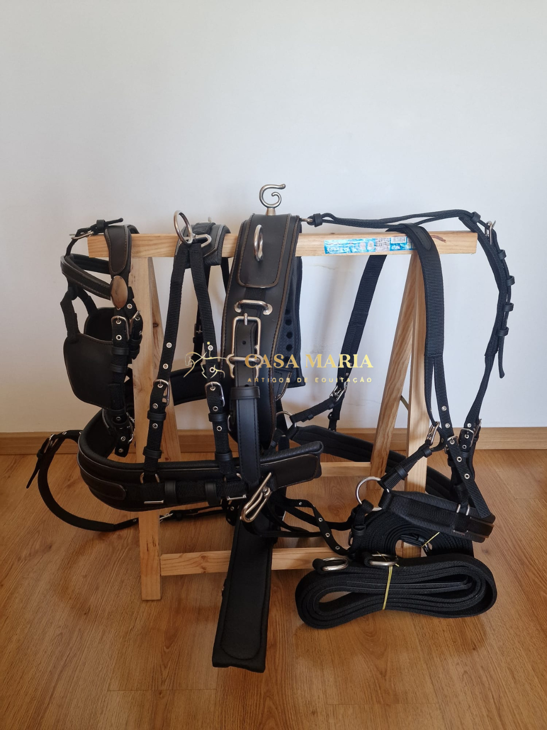 Equipamento e arreios para equitação em nylon e couro preto pendurados em suporte de madeira