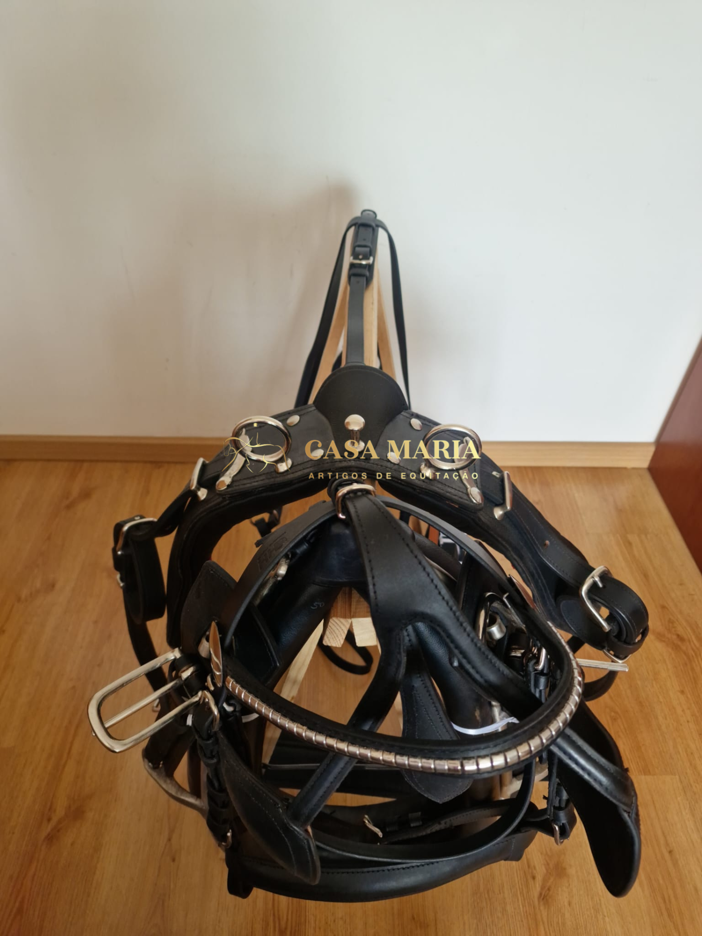 Arreio em couro preto com fivelas metálicas prateadas em suporte de madeira