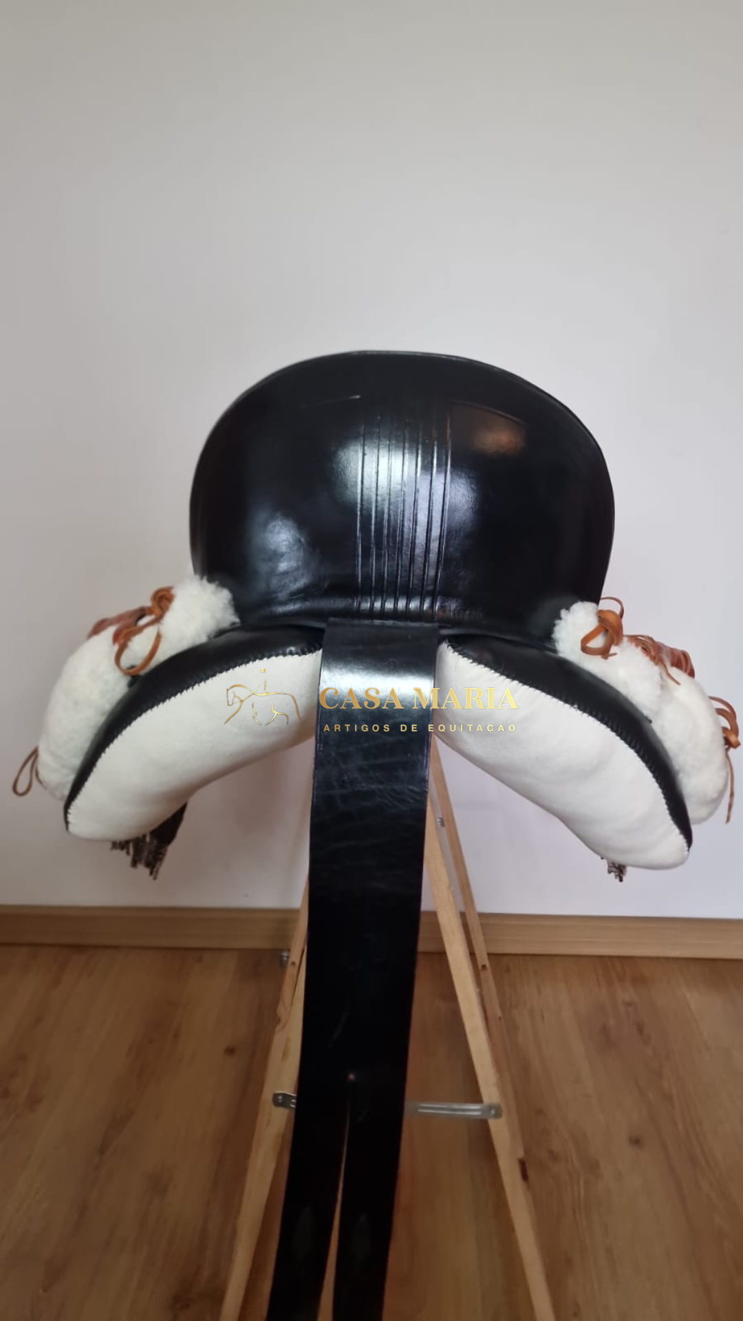 Sela de equitação preta com laterais brancas felpudas sobre suporte de madeira