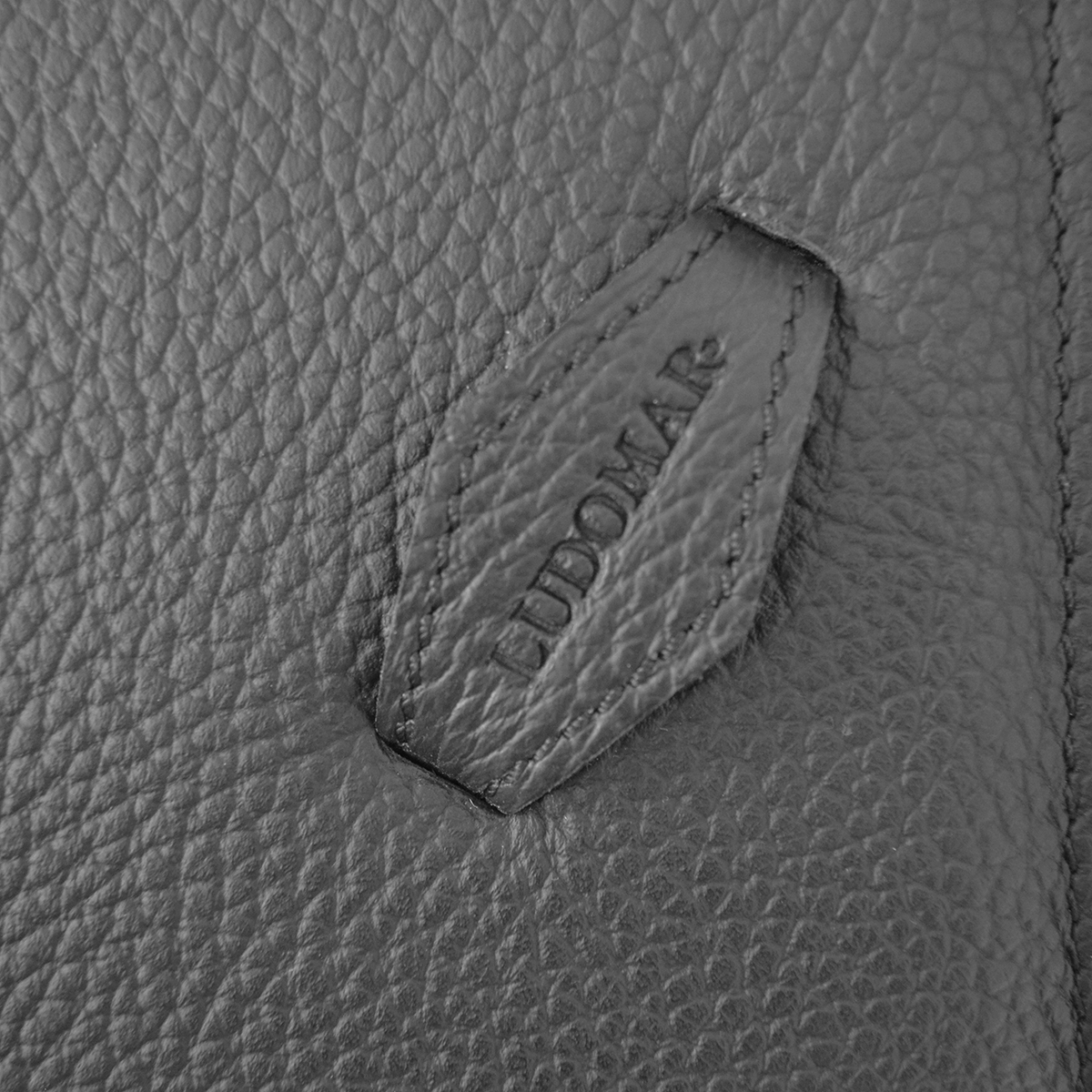 Etiqueta em pele preta com gravação 'LUDOMAR' em pele granulada preta