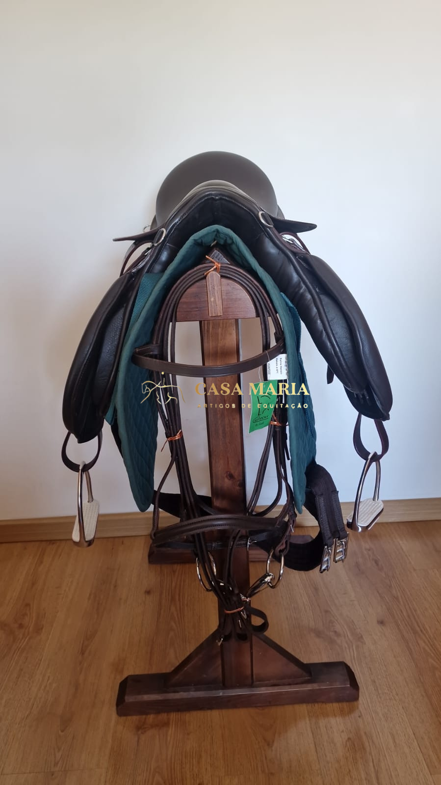 Sela de equitação de couro preto com almofada verde num suporte de madeira