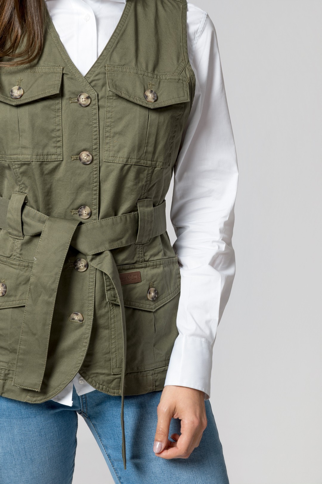 Colete verde estilo safari com botões e cinto usados sobre camisa branca e jeans azul