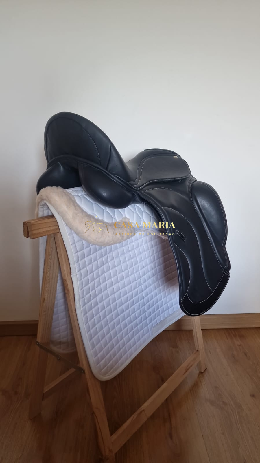 Sela de montar preta em couro sobre manta branca e suporte de madeira