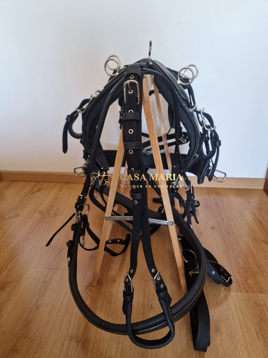 Conjunto de arreio preto para cavalo com fivelas e argolas em metal num suporte de madeira
