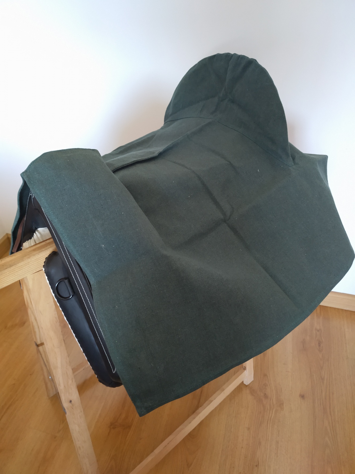 Sela de equitação preta coberta com tecido verde escuro sobre suporte de madeira