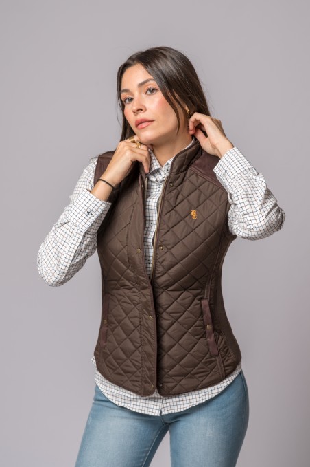 Mulher a usar colete castanho acolchoado com camisa branca de padrão xadrez e jeans