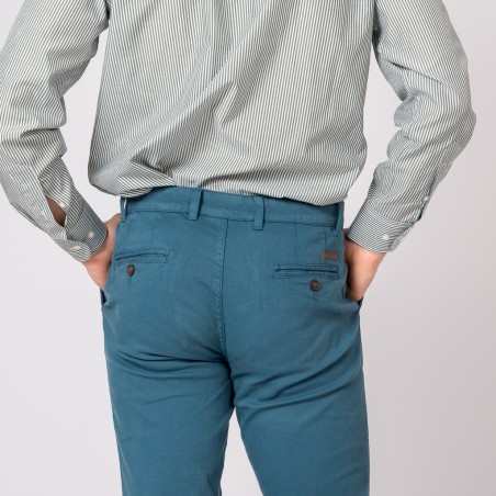 Calças azuis com bolsos abotoados e cinto usadas com camisa de riscas cinzentas.