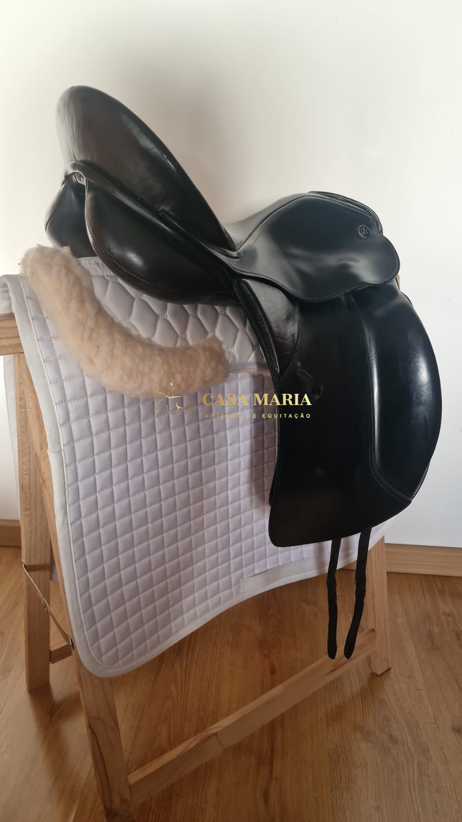 Sela de equitação preta em couro sobre suporte de madeira com manta branca acolchoada e forro de pelos