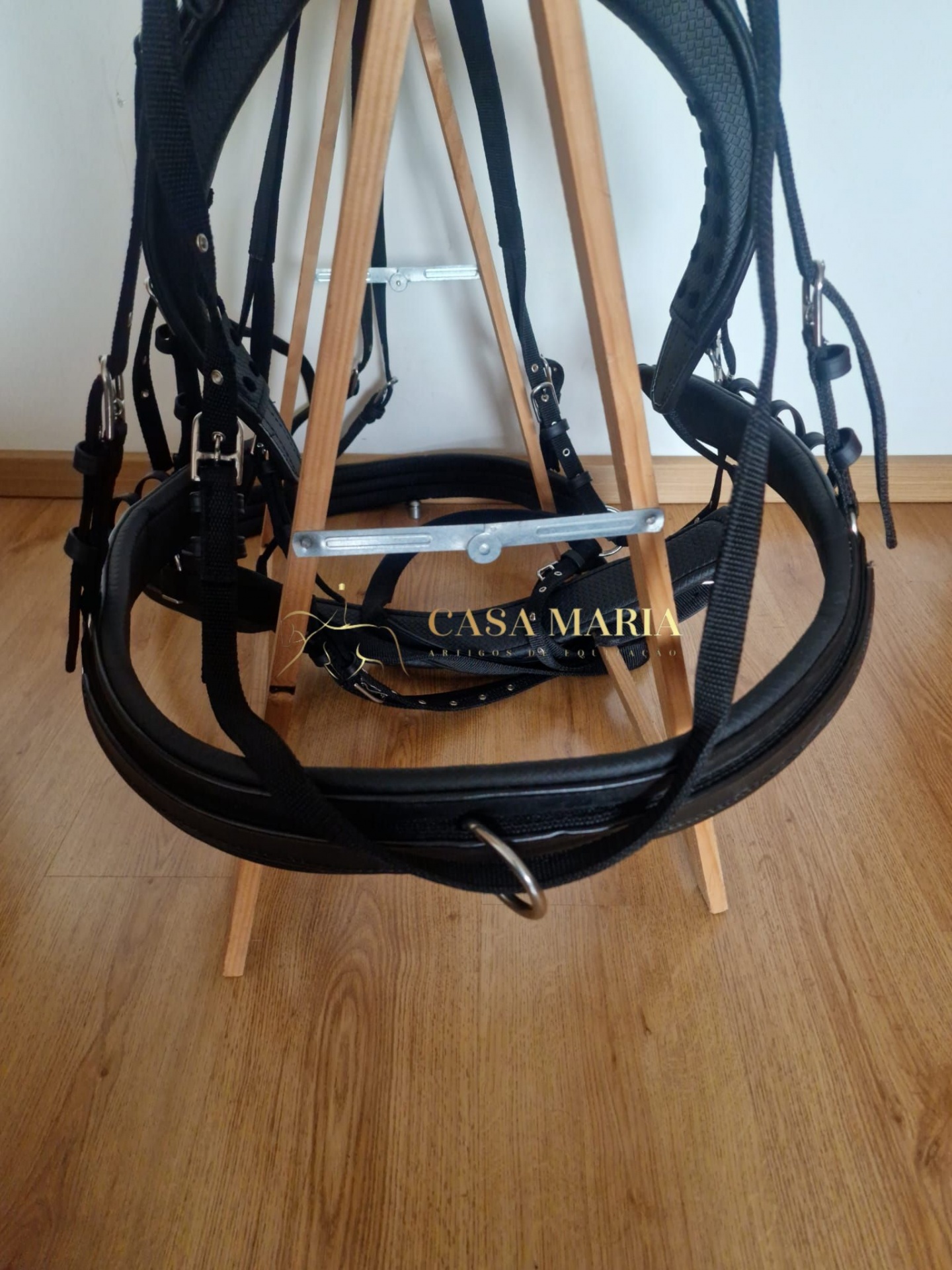 Embocadura e cabeçada preta de material sintético penduradas num cavalete de madeira.