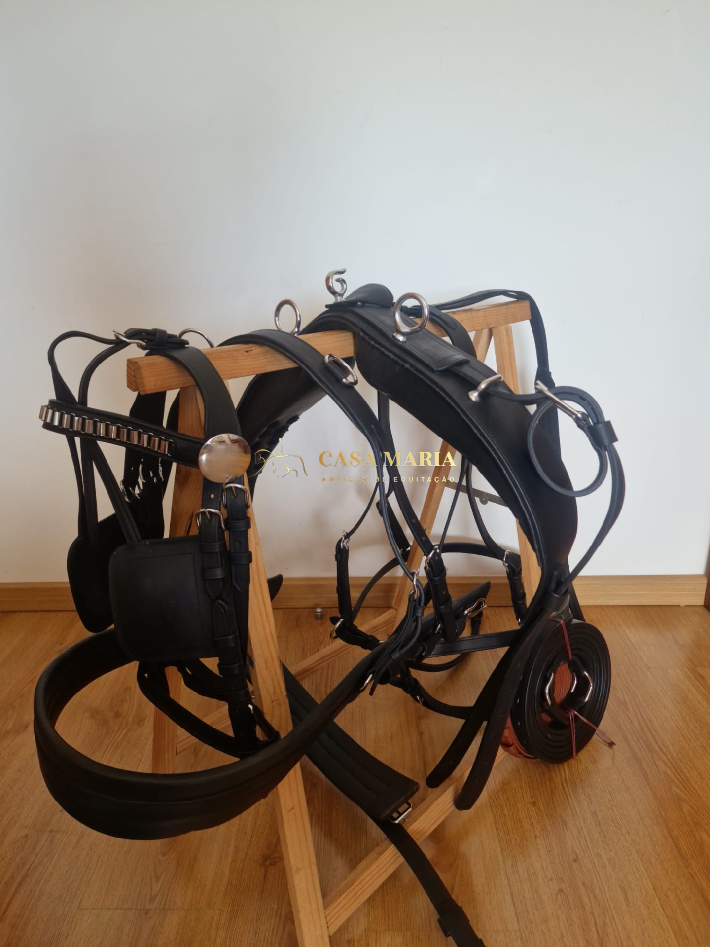 Arreio para cavalo em couro preto com fivelas metálicas sobre suporte de madeira