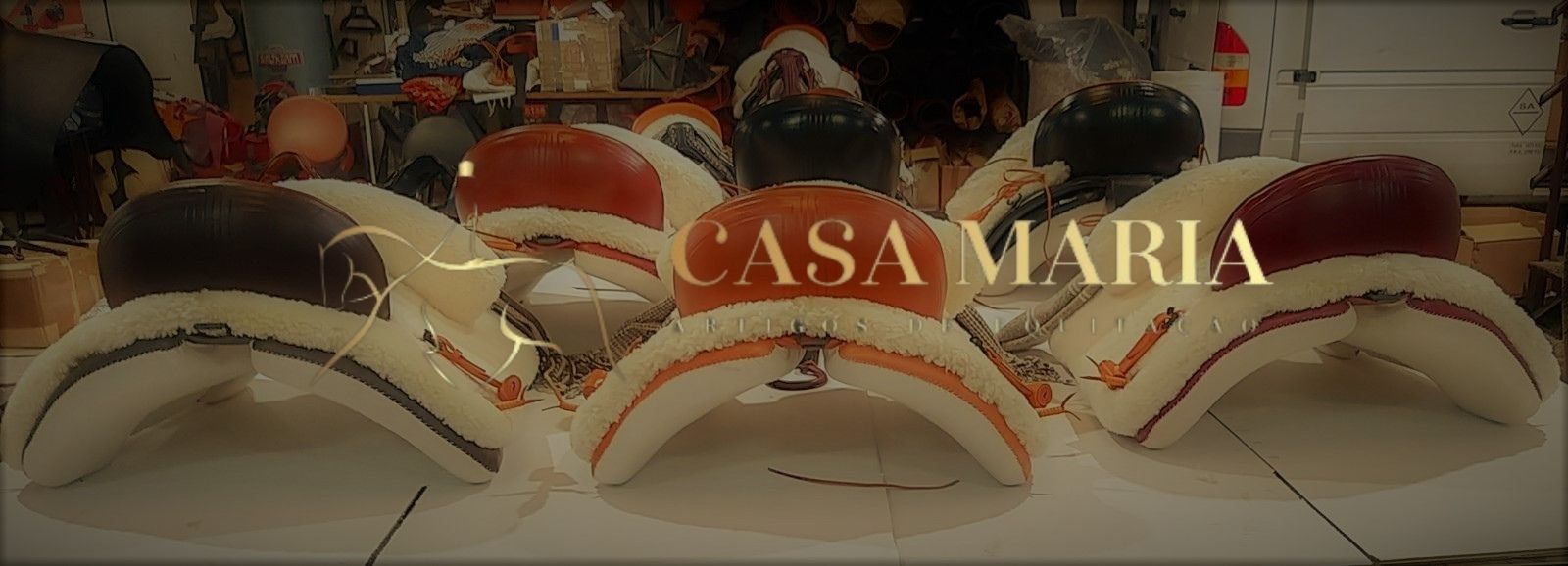 Seis selas de montaria em couro branco com detalhes castanhos, uma com texto 'CASA MARIA' em dourado